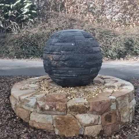 Multi-textured basalt sphere on a round sandstone plinth in a garden