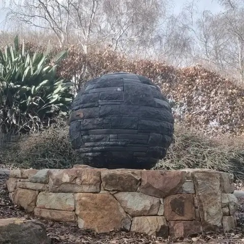 Multi-textured basalt sphere on a round sandstone plinth in a garden (2 of 3)