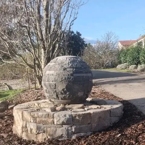 Multi-textured basalt sphere on a round sandstone plinth in a garden (3 of 3)