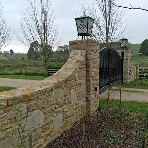 Curved sandstone entrance wall and stone pier beside a dark gate